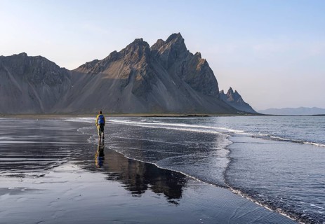 Tourist at black lava beach, sandy beach and sea, mountains Klifatindur reflected in the water,