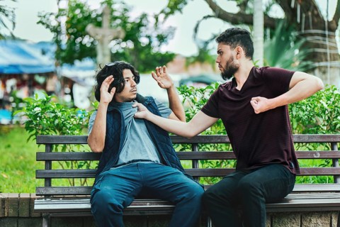 Two male friends arguing on a park bench. Two guys arguing sitting on a bench