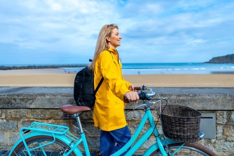 Tourist walking with her bicycle along the beach promenade on a cloudy day, enjoying the seascape