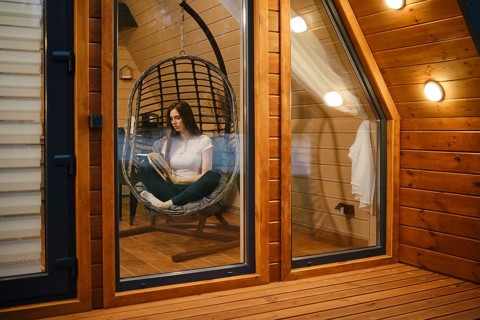 Cute woman sitting in a hanging swing chair and reading a book in the evening