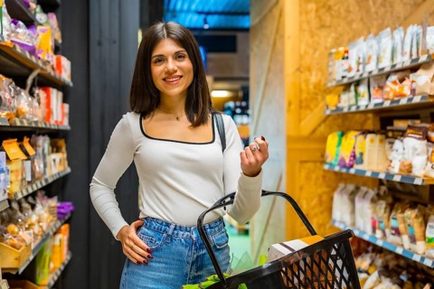 Young woman smiling and choosing organic products in a supermarket, holding a shopping basket