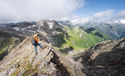 Mountaineer on a steep rocky ridge, on the summit of the Lasörling, view of the mountain panorama
