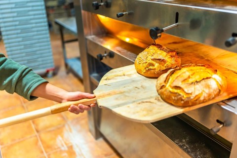 Latin unrecognizable man removing baked artisan bread from oven in a bakery kitchen