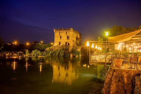 Night shot of restaurant on the Mincio river and Visconti bridge from 1395 in the background,