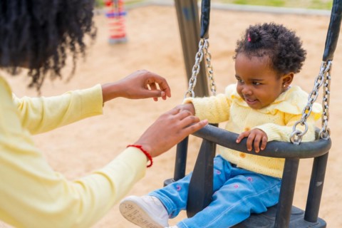 Close-up of a happy little african girl swinging with her mother in a park