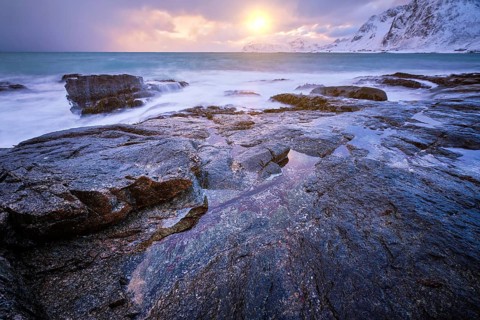 Beach of Norwegian sea on rocky coast in fjord on sunset in winter. Vareid beach, Lofoten islands,