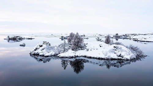 Snow-covered small islands overgrown with bushes in Lake Myvatn, at blue hour, Kalfaströnd, drone