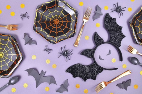Halloween party flat lay with spider web plates, costume bat headband, spiders and confetti on