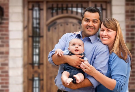 Happy mixed-race couple with baby in front of house