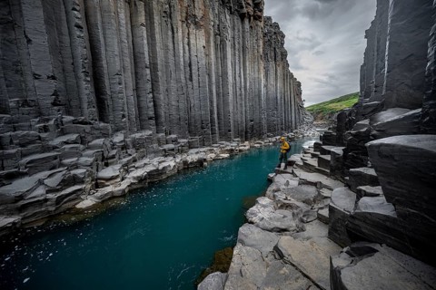 Tourist standing by the river in Stuðlagil Canyon, turquoise blue river between basalt columns,