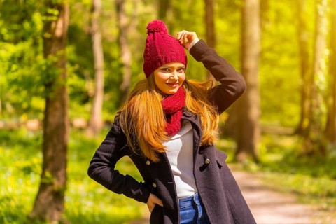 Latin girl with a black jacket, scarf and red woolen hat enjoying in an autumn park, smiling