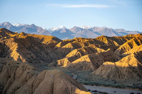 Landscape of eroded hills at sunrise, badlands, white mountain peaks of the Tian Shan Mountains in