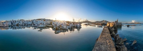Panorama, fishing boats in the harbour of Naoussa at sunset, reflected in the sea, sun star, ruins