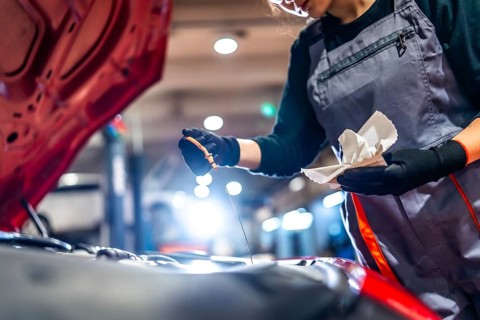 Professional female mechanic inspecting engine oil level with dipstick and rag in a car repair shop