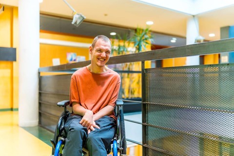 Happy man with cerebral palsy in a modern coworking smiling at camera in the corridor