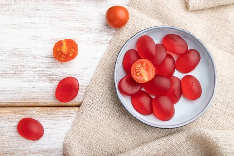 Jelly tomato candies on white wooden background and linen textile. close up, top view, flat lay