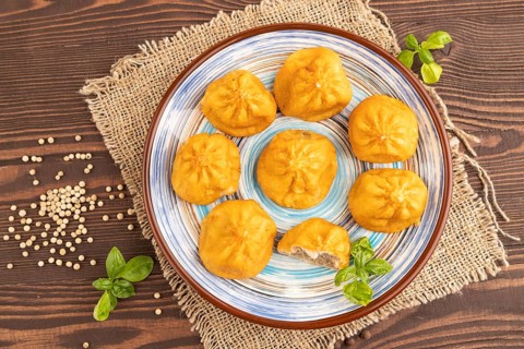 Fried manti dumplings with pepper, basil on brown wooden background and linen textile. Top view,