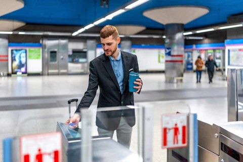 Businessman holding reusable coffee cup and using contactless credit card to enter subway station