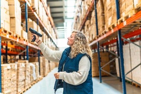 Side view of a blonde caucasian adult woman tracking packages using scan reader in a warehouse