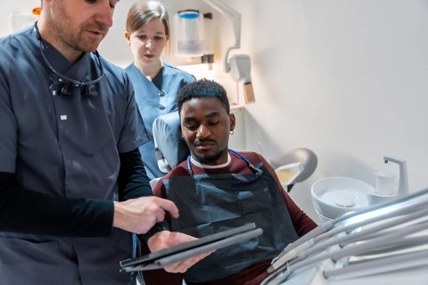 Dentist and nurse showing dental scan results on digital tablet to patient in modern clinic