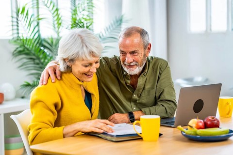 Senior man supporting his wife while doing household finances using laptop and notes