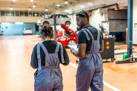 Two auto mechanics walking and reviewing notes on a clipboard in a professional garage, surrounded