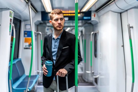Young businessman traveling by subway train, holding a reusable coffee cup and a trolley bag,