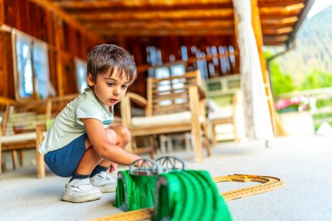 Young boy playing with a toy train set on a porch of a wooden cabin
