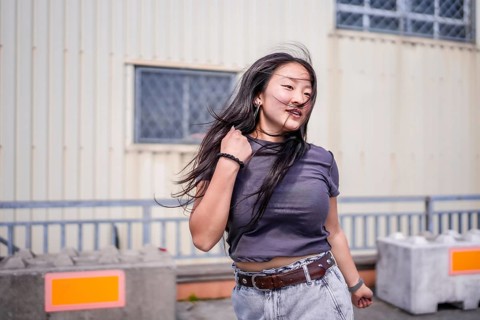 Three quarter length photo of a young cool asian girl dancing k-pop outdoors in an industrial
