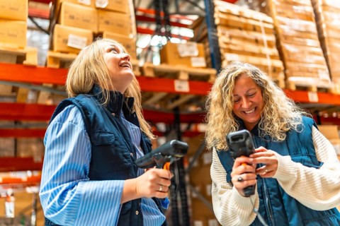 Happy blonde two female workers scanning boxes in a distribution warehouse
