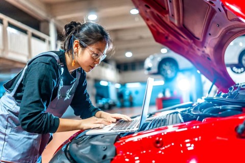 Young female mechanic using a laptop while inspecting a car engine in a professional auto repair