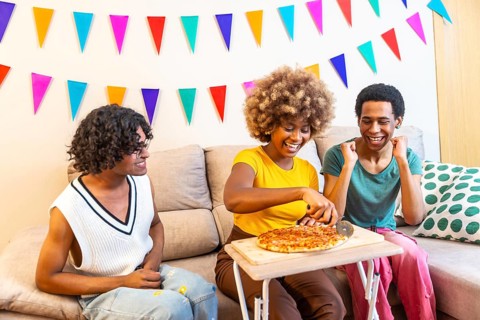 Multi-ethnic friends cutting and sharing pizza at home during party