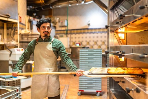 Male latin baker working removing tasty puff pastries from a traditional oven using peel