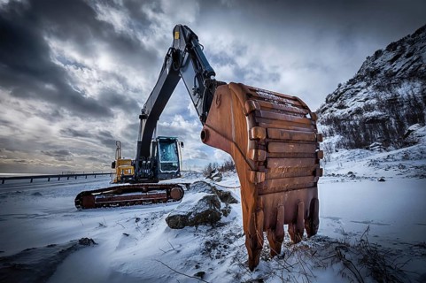 Old excavator with excavator bucket in winter. Road construction in snow. Lofoten islands, Norway.