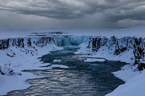 Selfoss waterfall with the river Jökullsa a Fjöllum, icy and snow-covered cliffs and shoreline,