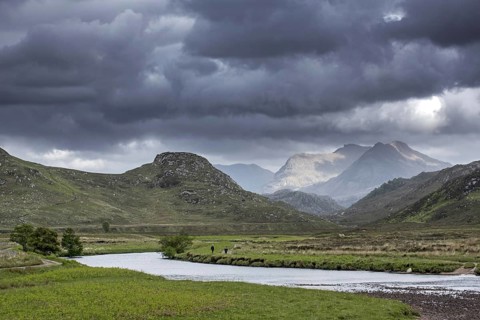 Two walkers walking on path along river and rain clouds forming in Wester Ross, Scottish Highlands,
