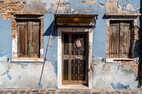 Dilapidated blue house facade with entrance door and windows, colourful houses on the island of