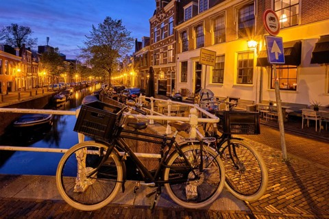 Typical Netherlands cityscape, bycicle at canal with boats and houses illuminated in the evening.