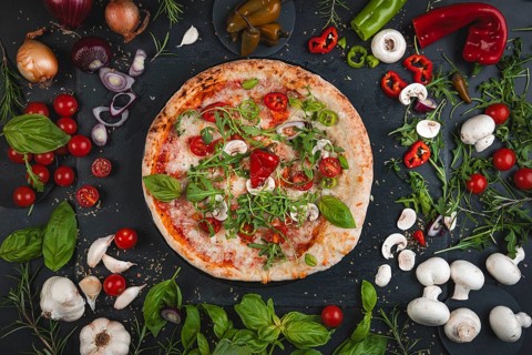 Colourful pizza topped with basil, tomatoes, rocket and mushrooms surrounded by ingredients