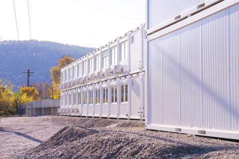 Row of white containers along a gravel path, illuminated by sunlight, refugee accommodation