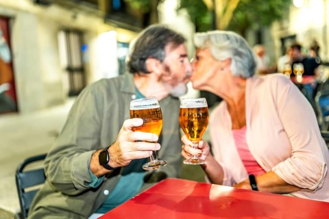 Senior couple kissing while toasting with beer in an outdoor terrace in the city