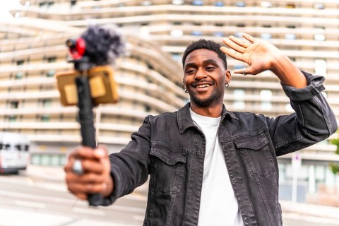 Young African man waving while filming a video blog in the city