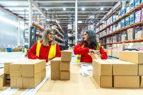 Happy female caucasian manual workers organizing boxes to ship in a distribution warehouse