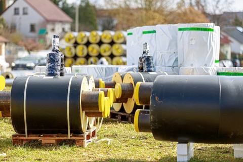 Stacked district heating pipes and district heating lines with yellow ends lie piled up in a meadow