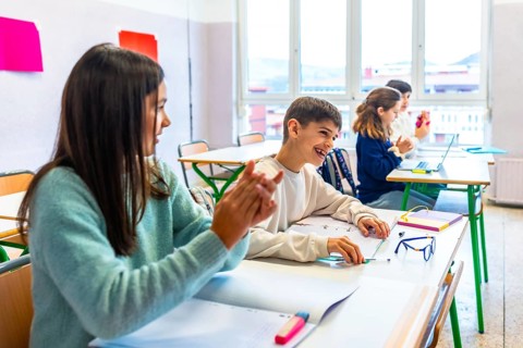 Happy elementary school students clapping hands in classroom, enjoying learning and having fun at