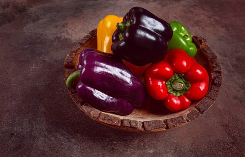 A collection of colorful bell peppers, in a wooden bowl, on a dark surface, top view, no people