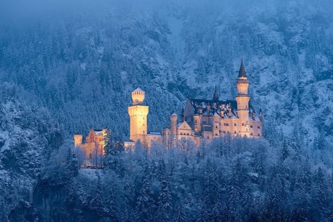 A majestic, illuminated castle in the middle of a snow-covered mountain landscape at night,
