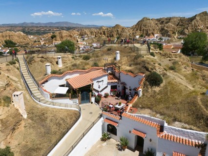 A white house with terracotta roof on a hill surrounded by nature and some people enjoying the