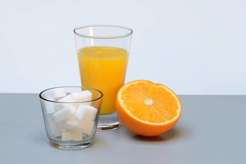 Orange juice in a drinking glass, half an orange and sugar cubes