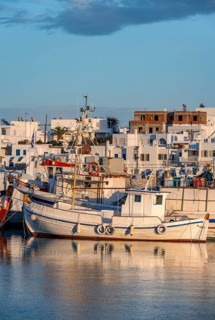 Fishing boats in the harbour at sunset, reflected in the sea, White Cycladic houses, Naoussa,